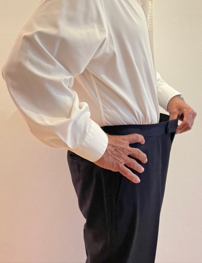 Man wearing a white dress shirt and dark pants against a plain background
